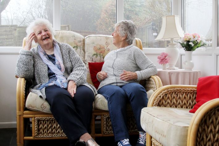 two women sitting in a conservatory laughing and smiling - Conservatory is warmer in the winter due to conservatory insulation