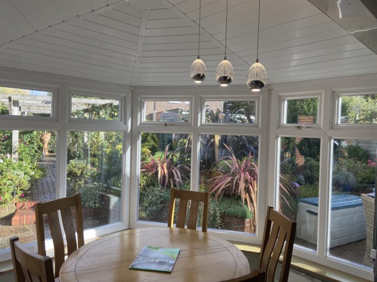 Conservatory with internal insulation, hanging center piece light and dining table.